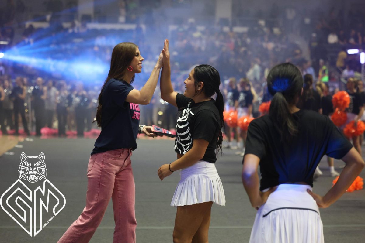 Lights flash around the school arena. Sophomore Myla Ray completes a standing full, she high-fives cheer coach Destine Grobe in celebration.
