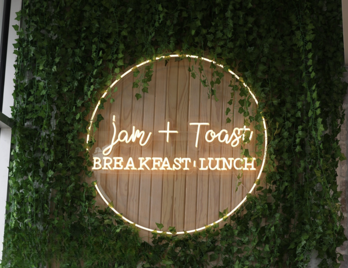 The Jam + Toast sign shines on an ivy covered wall. The sign is located at the front of the restaurant above a photo opportunity.