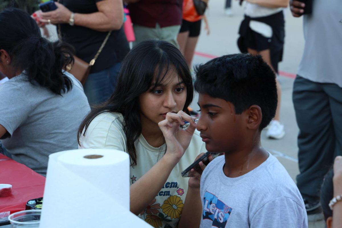 Fingers poised, Junior Deepshika Tulum, paints elementary students cheeks. Tulum volunteered at the Cockrell County Fair with NAHS.