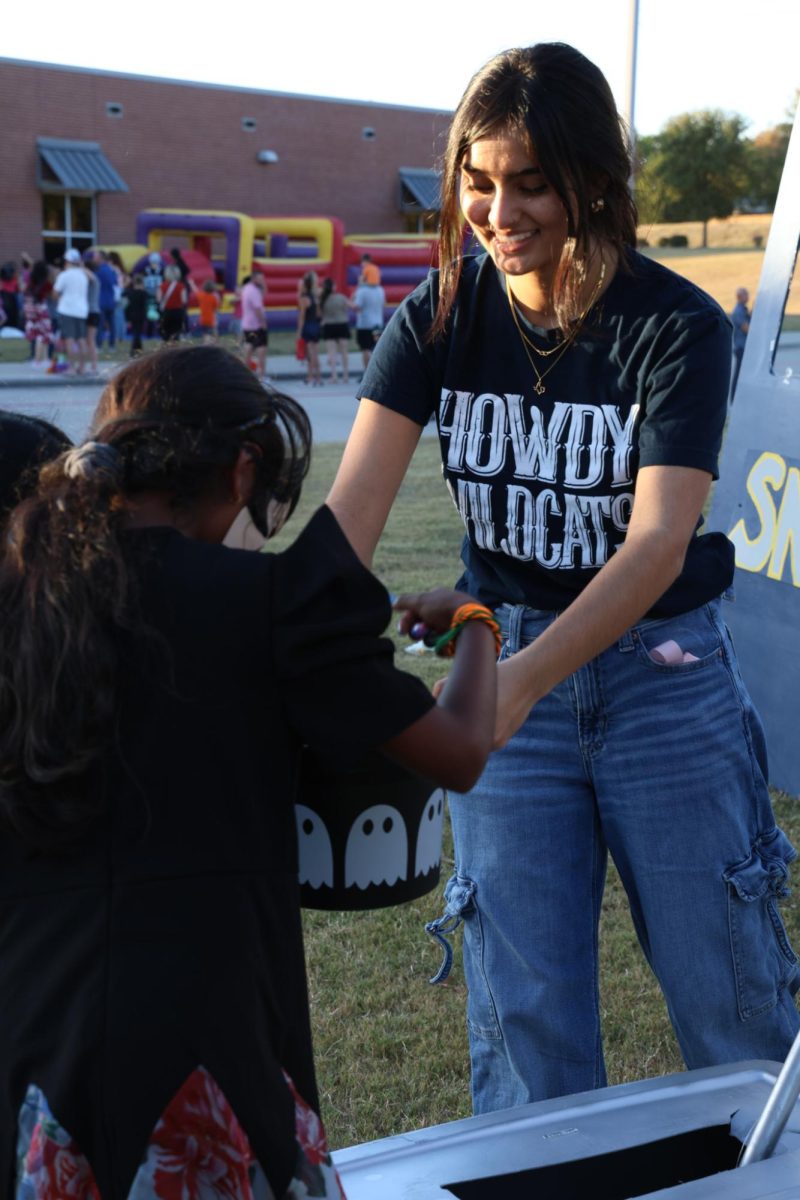 With a wide smile and outstretched arms, Junior Shaarika Kaul hands out candy to participants of Trunk-Or-Treat. Kaul volunteered with SNHS and ran a slot machine along with other members of the honors society.