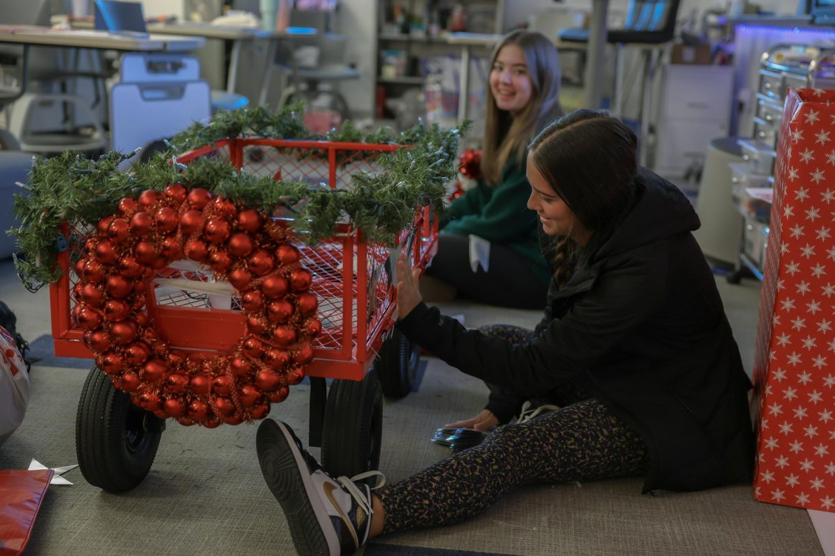 On the ground, Student Council Vice President Jocelyn Johnson and member Maylee Stankiewicz decorate the wagon student council will use in the parade. The parade will take place tomorrow at 11:45 during Grove Time. All toys and donations will be sent to Conerstone Church. 