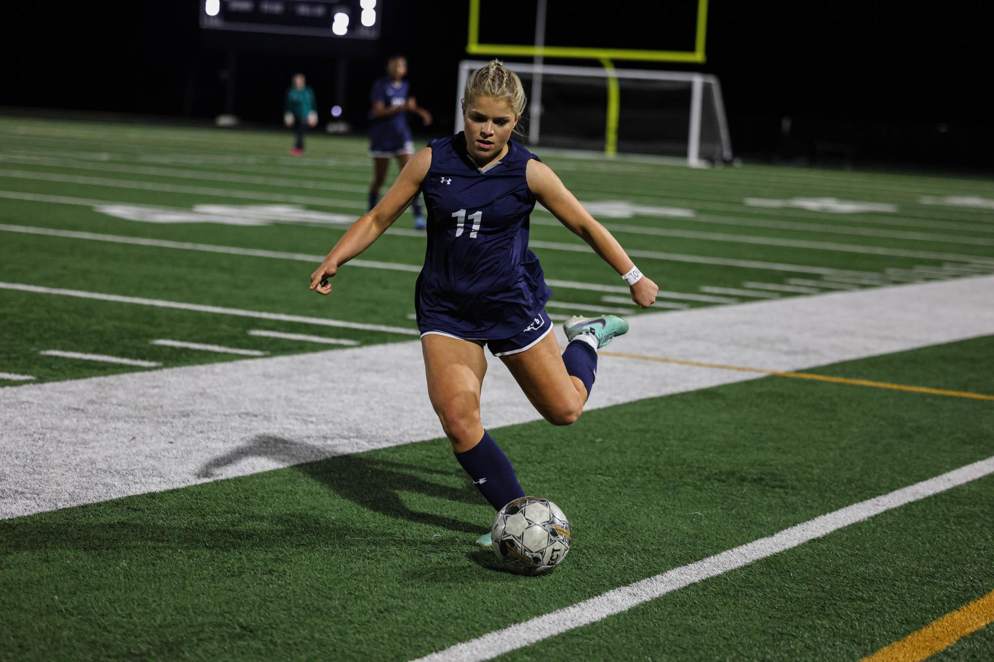 Player 11, Senior Lily Miller, kicks the soccer ball with power to the other side of the field. 