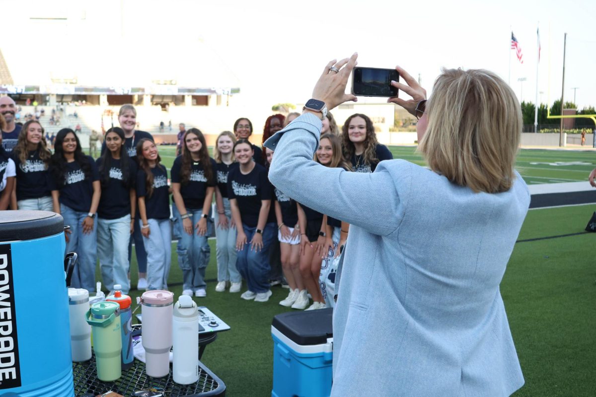 Arms raised, Superintendent Dr. Holly Ferguson takes a picture of the WGHS choir at a football game.